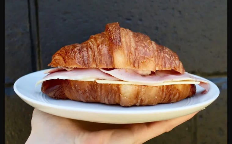 Bánh sừng bò nhân giăm bông phô mai vàng ruộm trên đĩa trắng, nền tường tối màu.