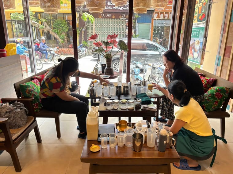 Ba vị khách quây quanh bàn thấp bày đầy dụng cụ pha chế trong lớp học tại Cam On Cafe.