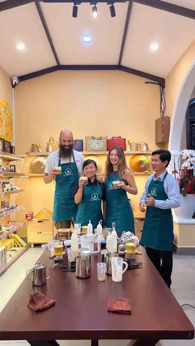 Du khách và người hướng dẫn trong tạp dề xanh cùng cầm ly cà phê tự pha tại Cam On Cafe.