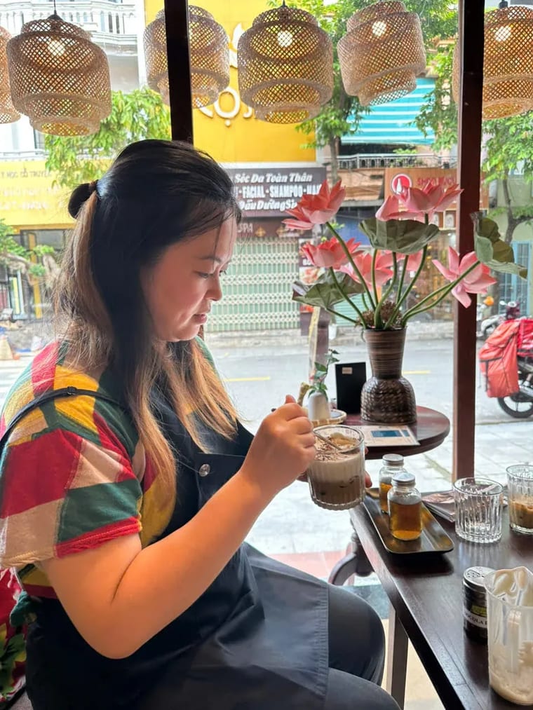 Một vị khách nữ mặc tạp dề khuấy ly cà phê tự pha trong buổi học tại Cam On Cafe.