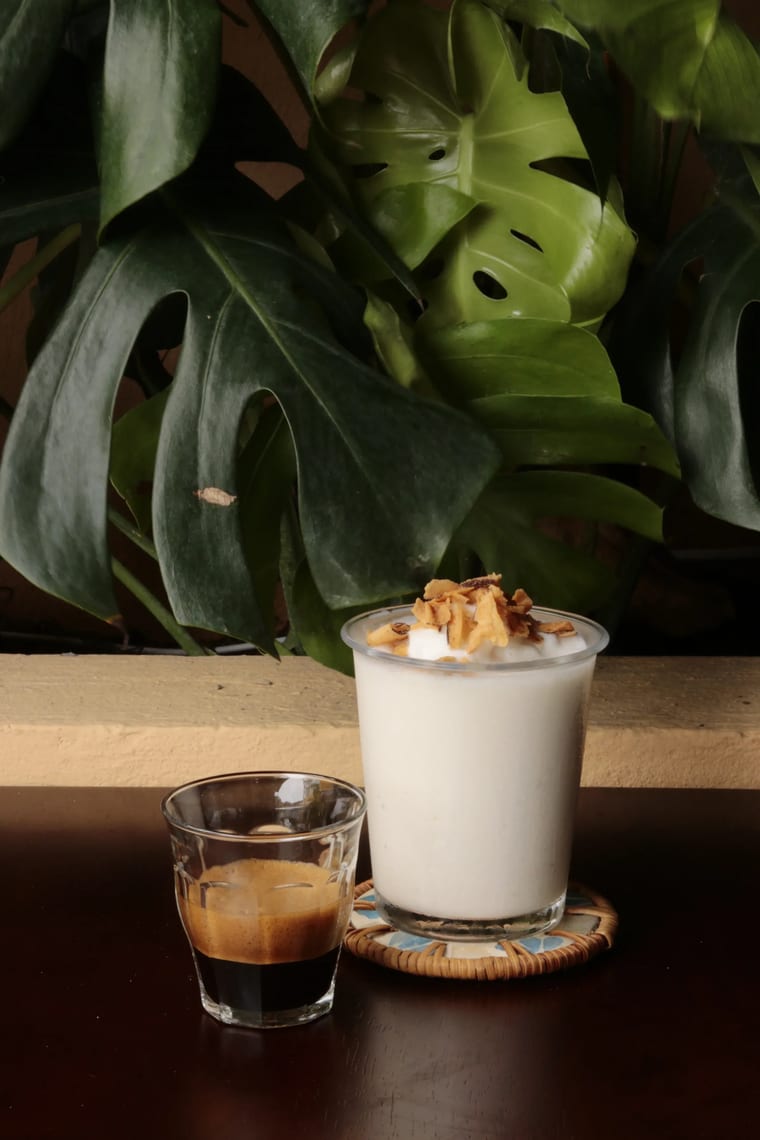 Ly sinh tố dừa đá rắc dừa nướng đặt cạnh một shot espresso tại Cam On Cafe.