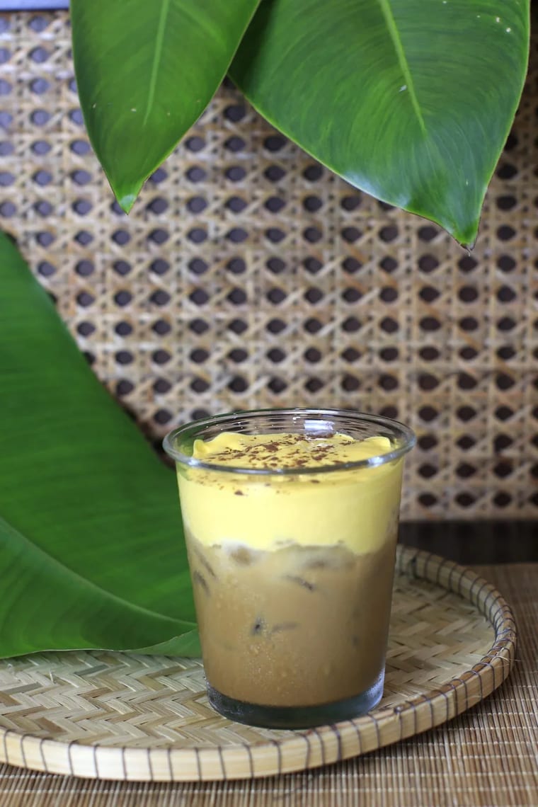 Ly cà phê trứng đá phục vụ trên khay đan, xung quanh là lá xanh.