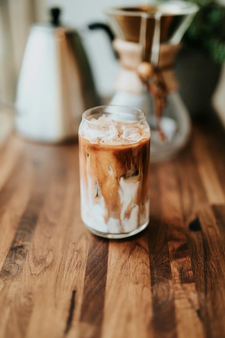 Ly thuỷ tinh trong đựng cà phê đá nhiều tầng, đặt trên quầy gỗ ấm màu tại Cam On Cafe.