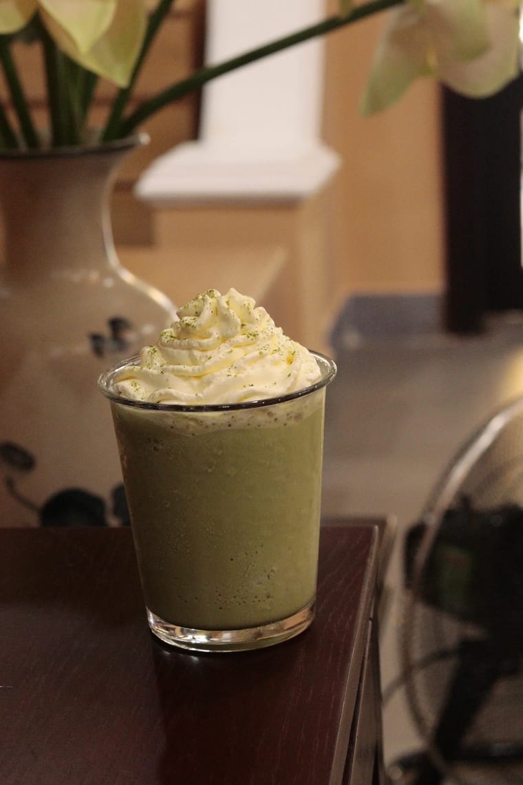 Matcha đá xay phủ kem tươi, đặt trên bàn gỗ tại Cam On Cafe.