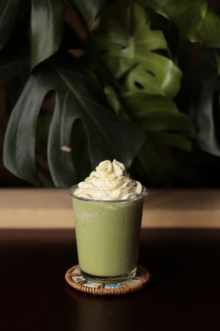 Ly matcha đá phủ kem tươi, đặt trên đế lót tại Cam On Cafe.