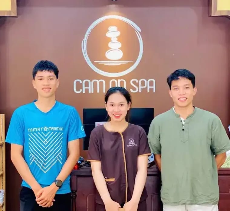 Ba người đứng chụp ảnh chung trước quầy lễ tân của Cam On Cafe.