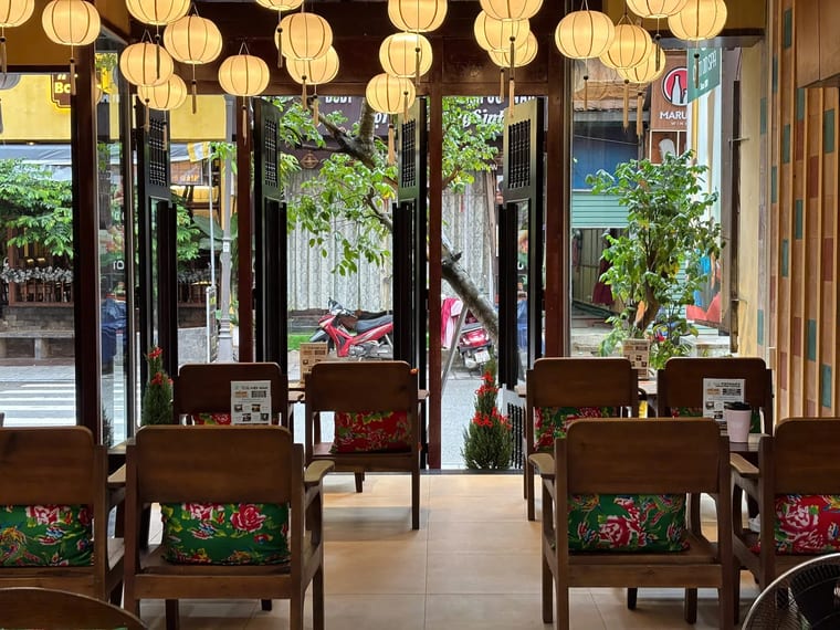 Không gian ấm cúng bên trong Cam On Cafe với ghế gỗ nệm hoa và đèn lồng treo.
