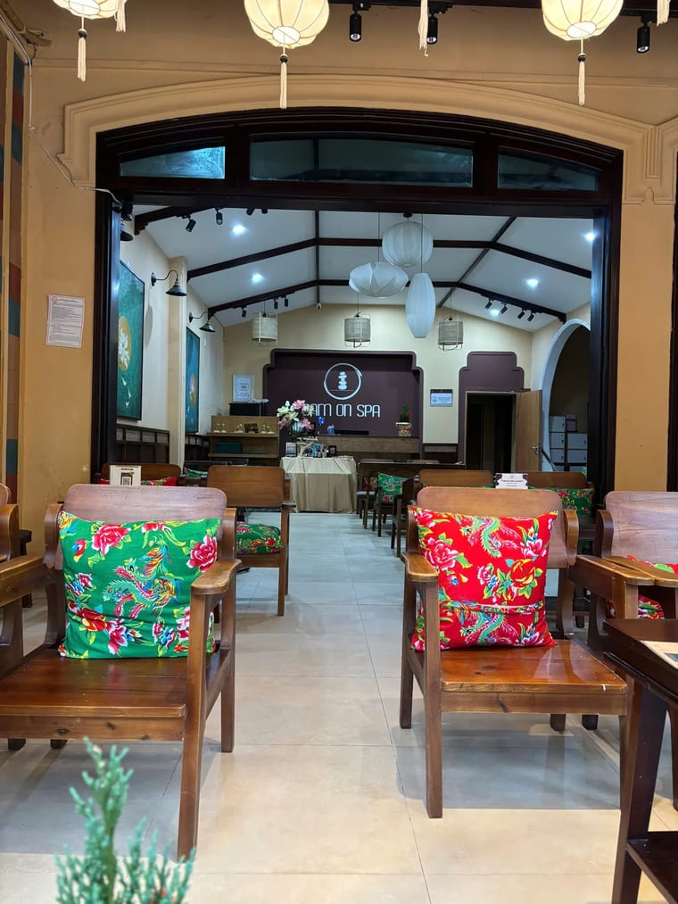 Góc ngồi ấm cúng bên trong với ghế bành gỗ và nệm hoa nhiều màu tại Cam On Cafe.
